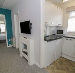 A hallway with a mounted television and a small kitchen with white cabinets and appliances at Hafod-y-Gors in Fairbourne