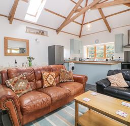 An open living room and kitchen area with brown and black leather sofas a wooden coffee table and kitchen cabinets at The Old Haybarn in Ipplepen