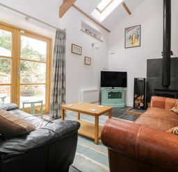 A living room with black and brown sofas a wooden coffee table a television and a wood burning stove at The Old Haybarn in Ipplepen