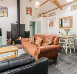 A living room with a leather sofa a wood stove and a dining table at The Old Haybarn in Ipplepen
