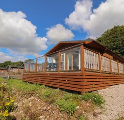 A row of wooden cabins with glass and wood railings on raised decks surrounded by grass and trees at Mereside South lakeland Leisure Village near Carnforth