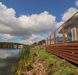 A lakeside view with wooden deck railing and houses along the shore at Mereside South lakeland Leisure Village near Carnforth