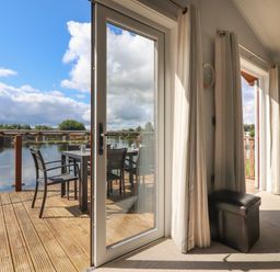 A room with large glass doors opening to a wooden deck with a table and chairs overlooking water at Mereside South lakeland Leisure Village near Carnforth