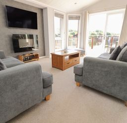 A living room with two grey sofas a wooden coffee table a wall mounted tv and a fireplace at Mereside in South lakeland Leisure Village near Carnforth