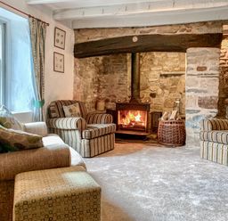 A living room with a wood-burning stove stone walls armchairs and a window at The Farmhouse in Newport Pembrokeshire