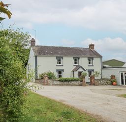 A two-story house with white walls and gray trim surrounded by plants and a gravel driveway at The Farmhouse in Newport Pembrokeshire