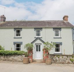 A two story house with a white door and four windows surrounded by plants and brick pillars at The Farmhouse in Newport Pembrokeshire