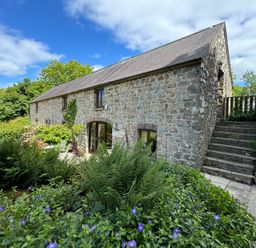 A stone cottage with a slate roof surrounded by plants and flowers with stairs on the side at Stable Cottage in Newport Pembrokeshire