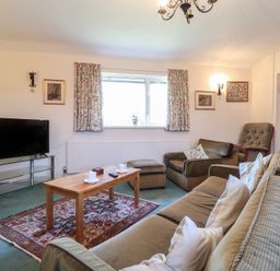 A living room with sofas a wooden coffee table a television and a window with curtains at Otter Cottage in Dinas Cross