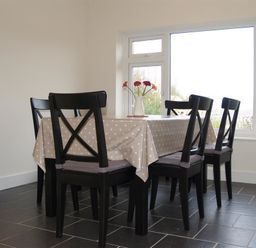 A dining area with a table covered by a polka dot tablecloth and six black chairs near large windows at Gellifor in St Dogmaels Pembrokeshire