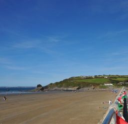 A sandy beach with people on it and a promenade with benches and flags at Seabrook Broad Haven Pembrokeshire
