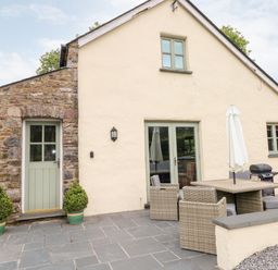 Exterior view of a stone and plaster house with green door and window frames patio with outdoor dining table chairs and umbrella at Gwyddno Lodge in Narberth Pembrokeshire
