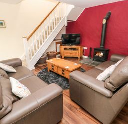 A living room with two brown sofas a wooden coffee table a TV on a wooden stand a wood burning stove and stairs at Gwyddno Lodge in Narberth Pembrokeshire