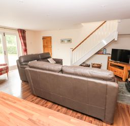 A living room with leather sofas a TV under stairs and a wood burning stove at Gwyddno Lodge in Narberth Pembrokeshire