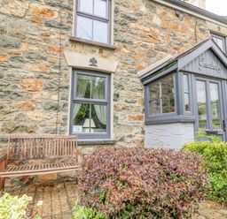 Stone house exterior with wooden bench shrubbery and enclosed porch at Greenbanks in Dinas Cross Pembrokeshire