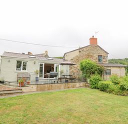 A backyard with a green lawn and a patio area next to a house with stone and plaster walls at Greenbanks in Dinas Cross Pembrokeshire