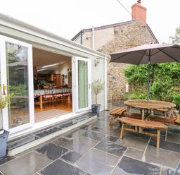 An outdoor patio with black tiled floor a wooden picnic table with umbrella and potted plants outside French doors at Greenbanks in Dinas Cross Pembrokeshire