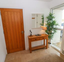 An entryway with a wooden door a white door with glass a wooden console table with drawers a lamp a potted plant and a wall mirror at Gwelfor Marloes in Marloes Pembrokeshire