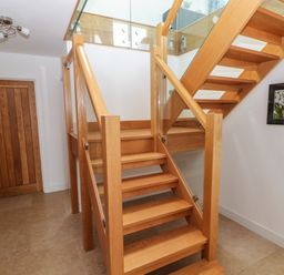 A wooden staircase with glass panels in a hallway with a wooden door and a framed picture on the wall at Gwelfor Marloes in Marloes Pembrokeshire