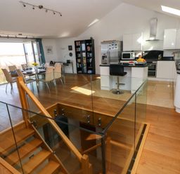 An open plan kitchen and dining area with a glass railing stairwell and a dining table with chairs at Gwelfor Marloes in Marloes Pembrokeshire