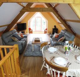 An attic living area with two sofas a coffee table a television a dining table set for four and exposed wooden beams at Pond Cottage in New Quay Ceredigion