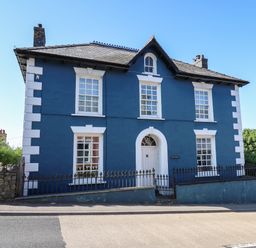 A blue two story house with white window frames and a white door behind a black iron fence Dewi Villa Aberarth Ceredigion