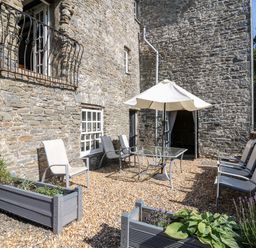 An outdoor patio with stone walls glass table white umbrella and chairs at Dewi Villa in Aberarth Ceredigion