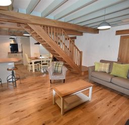 An open plan living area with wooden staircase gray sofa armchair coffee table and kitchen bar stools at The Old Farmhouse Kitchen in St Davids Pembrokeshire
