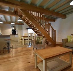 An open living area with wooden staircase wooden stools dining table chairs and a sofa with cushions at The Old Farmhouse Kitchen in St Davids Pembrokeshire