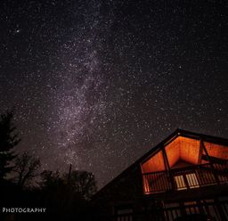 A night sky filled with stars above a lit balcony of a wooden house at Dan Castell Cottage in Llandeilo Carmarthenshire