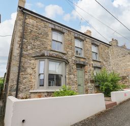 A stone exterior house with three windows and a green door with white fences at Nevern House in Newport Pembrokeshire