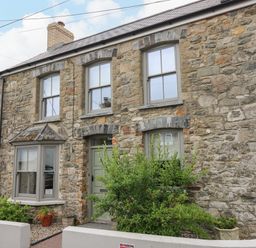 Stone exterior of a two story house with three windows a green door and plants by the entrance at Nevern House in Newport Pembrokeshire
