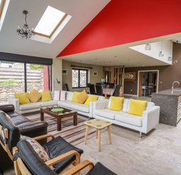 An open living room and kitchen area with white sofas yellow cushions glass coffee table dining table and chairs at Nevern House in Newport Pembrokeshire