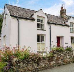 A detached cottage with a stone wall and flowers in front at Panteg Cottage Newport Pembrokeshire
