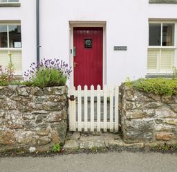 A front entrance with a red door white picket gate and stone walls with plants at Panteg Cottage Newport Pembrokeshire