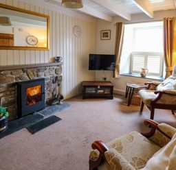 A living room with a stone fireplace a TV on a stand two armchairs and a window with curtains at Panteg Cottage Newport