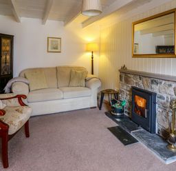 A living room with a beige sofa a floral armchair a stone fireplace and a floor lamp at Panteg Cottage Newport