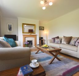 A living room with two beige sofas a wooden coffee table with fruit and a fireplace at Greenfields in St Davids Pembrokeshire