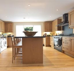A kitchen with wooden cabinets a kitchen island with chairs a refrigerator and a stove at Gwelfor Newport in Newport Pembrokeshire