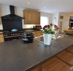 A kitchen with wooden cabinets a black stove a countertop with a sink flowers in a vase and wooden stools at Gwelfor Newport in Newport Pembrokeshire