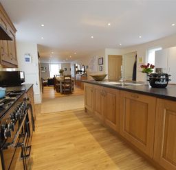 A kitchen with wooden cabinets a black countertop a stove and a sink with a dining area in the background at Gwelfor Newport in Newport Pembrokeshire