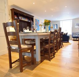 A dining room with a long table and wooden chairs a dark wooden cabinet and a living area in the background at Gwelfor Newport in Newport Pembrokeshire