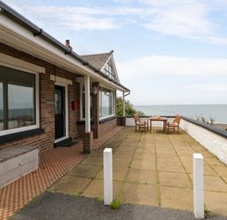An outdoor patio with a table and chairs overlooking the sea at Delyn Aur, Tresaith, Ceredigion