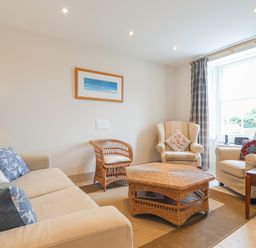 A living room with a sofa armchairs wicker coffee table and window with curtains at Neverndale Newport Pembrokeshire