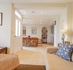 A living room with a beige sofa and a wicker ottoman leading to a dining area with a wooden table and chairs at Neverndale in Newport Pembrokeshire