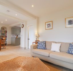 A living room with a beige sofa and blue pillows next to a wooden dining table and a bookshelf at Neverndale in Newport Pembrokeshire