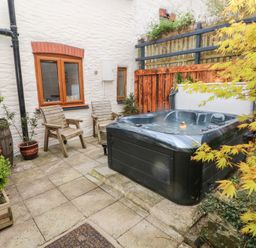 An outdoor patio with a hot tub two wooden chairs potted plants and a wooden fence at Mill Barn Denant in Haverfordwest Pembrokeshire