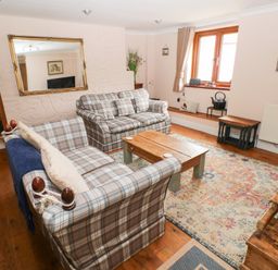 A living room with plaid sofas a wooden coffee table a large mirror and a patterned rug at Mill Barn Denant in Haverfordwest Pembrokeshire