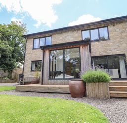 The back of a two-story stone house with large windows wooden deck steps and garden with grass and plants at Ty Cerrig in Newport Pembrokeshire