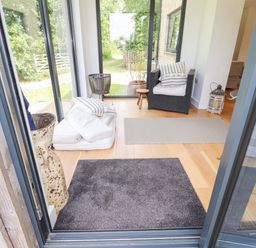 A seating area with a wicker chair cushions rugs and large windows showing a garden at Ty Cerrig Newport Pembrokeshire